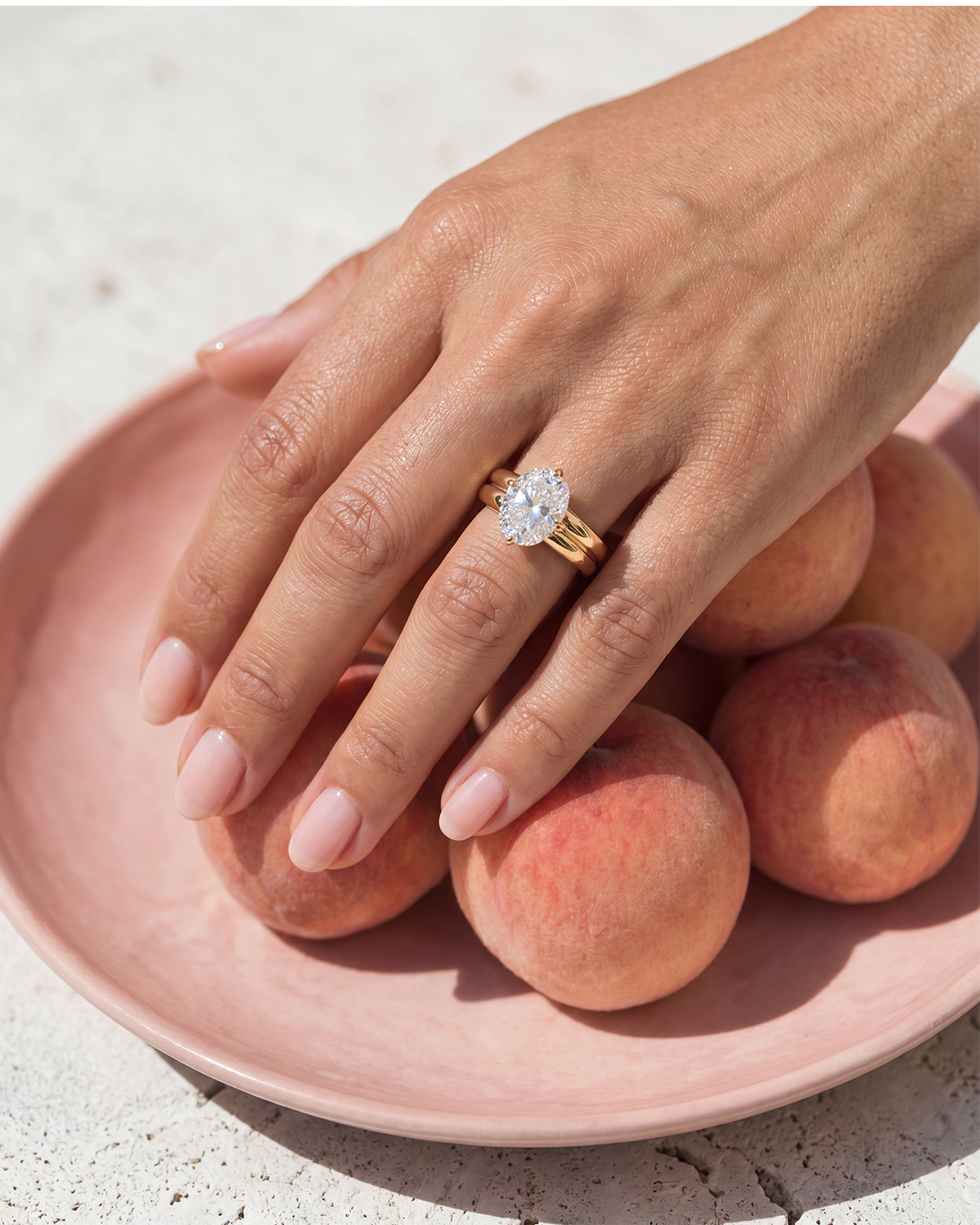 woman in green wearing a large oval diamond ring with a halo in yellow gold with white background