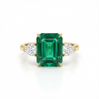 Gold ring with a green emerald and two diamonds on a white background