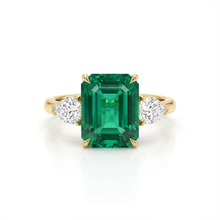 Gold ring with a green emerald and two diamonds on a white background