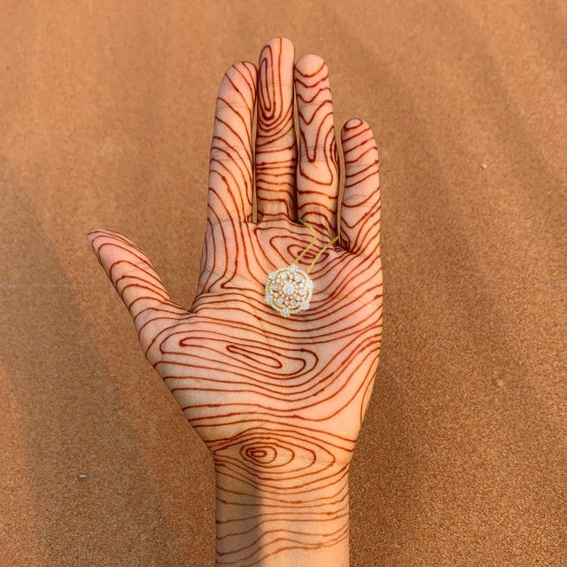 Hand with intricate henna design holding a decorative ring against a brown background