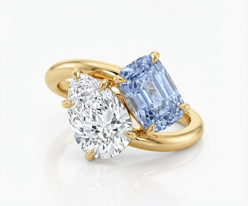 Gold ring with two diamonds, one white and one blue, on a light background