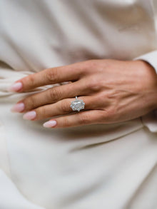 Close-up of a hand wearing a diamond ring on a light fabric background