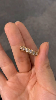 Gold fully eternity lab diamond wedding band held between fingers against a dark background