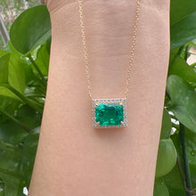 Gold necklace with a green emerald pendant on a person's wrist against a green leafy background