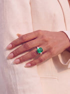 Hand wearing a ring with an emerald on a light background