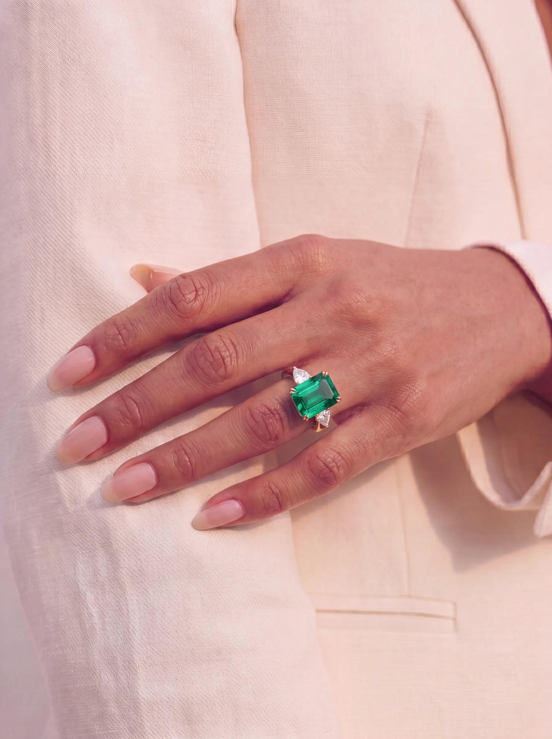 Hand wearing a ring with an emerald on a light background