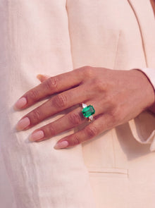Hand wearing a ring with an emerald on a light background