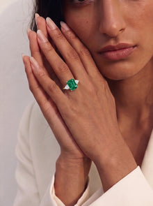 Close-up of a woman's hand wearing an emerald ring with a white background