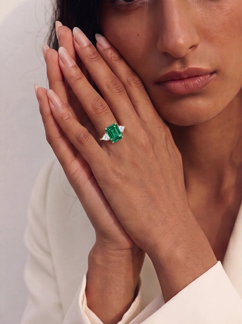 Close-up of a woman's hand wearing an emerald ring with a white background