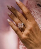 Hand wearing a pink diamond ring with a soft pink background