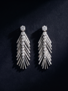 Pair of white gold palm leaf earrings with a diamond on a black background