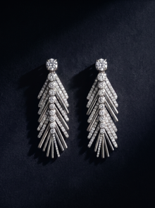 Pair of white gold palm leaf earrings with a diamond on a black background