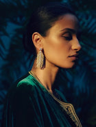 Woman wearing gold palm leaf earrings with a dark background