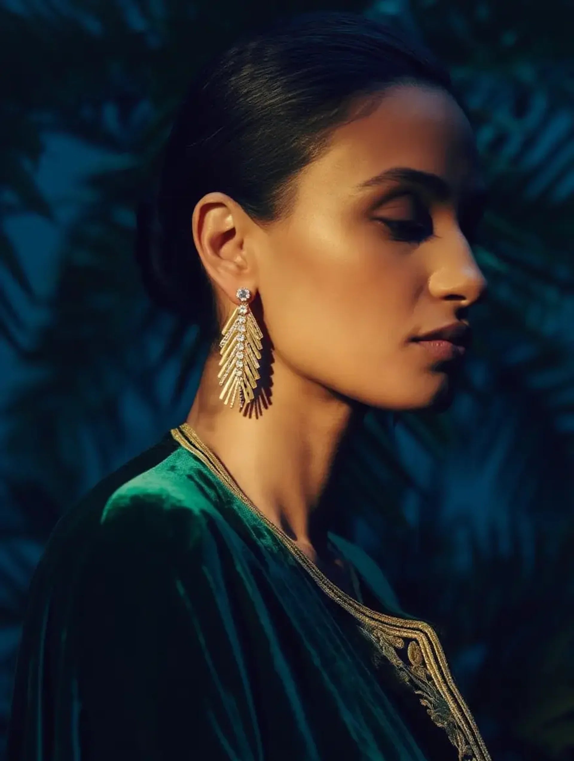 Woman wearing gold palm leaf earrings with a dark background