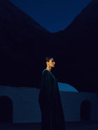 Woman in a green dress standing in front of a dark mountainous landscape