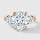 Rose gold ring with a large diamond and smaller diamonds on the sides against a light gray background