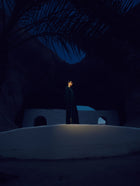 Person in a dark cloak standing in a desert landscape at night