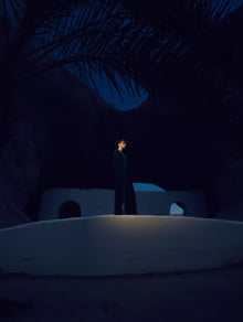 Person in a dark cloak standing in a desert landscape at night