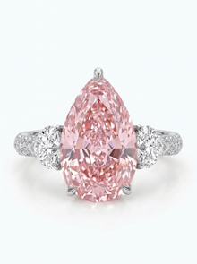 A pear-cut pink diamond ring with a silver-toned band accented by two round diamonds, set against a clean white background.