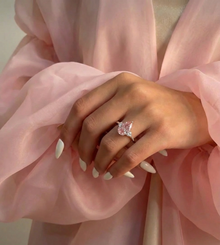 Hand wearing a pink diamond ring with a soft pink fabric background