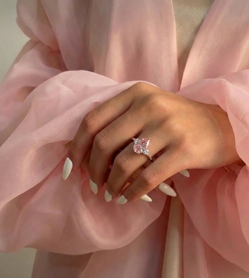 Hand wearing a pink diamond ring with a soft pink fabric background