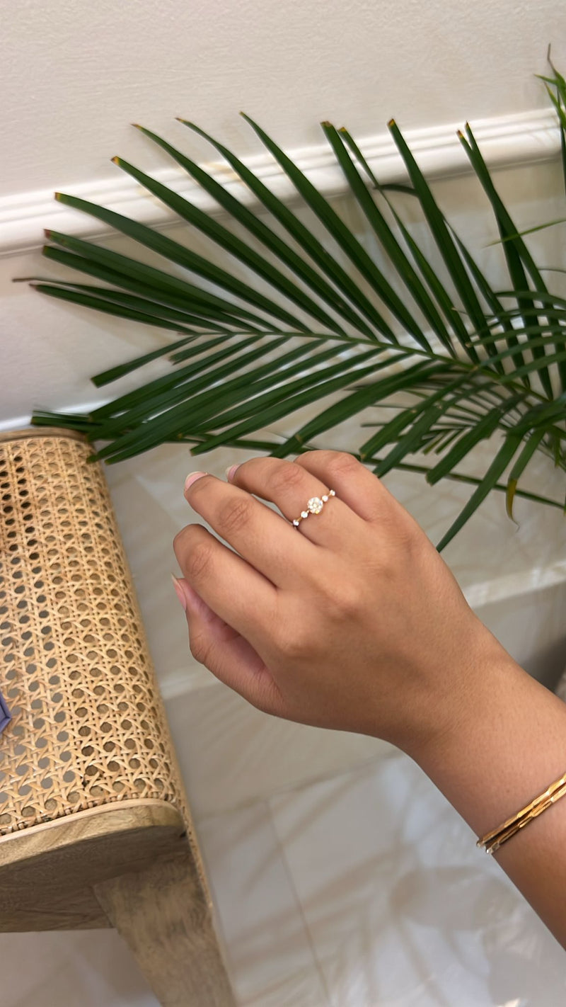 Hand wearing a ring with a plant in the background