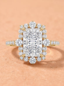 Diamond ring with a large central radiant cut diamond with a diamond halo on a peach background
