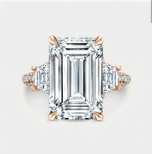 Diamond ring with emerald-cut center stone and rose gold accents on a light gray background
