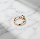 Rose gold ring with a green gemstone on a marble background