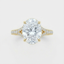 Gold ring with a large diamond and smaller diamonds on the band against a light gray background