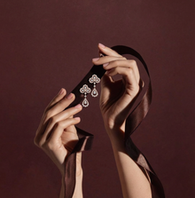Pair of hands holding a black box with diamond earrings against a dark red background