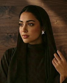 Woman wearing a sparkly, floral diamond earrings  a dark hijab against a wooden background
