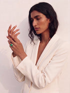 Woman wearing a white suit with a green ring on a plain background