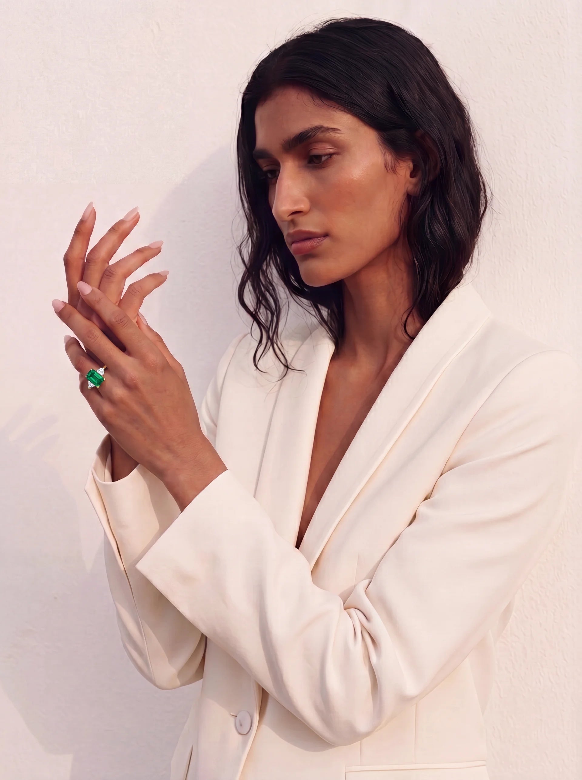Woman wearing a white suit with a green ring on a plain background
