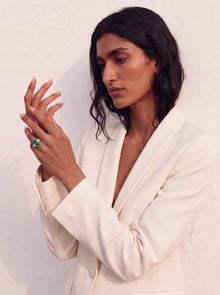 Woman wearing a white suit with a green ring on a plain background